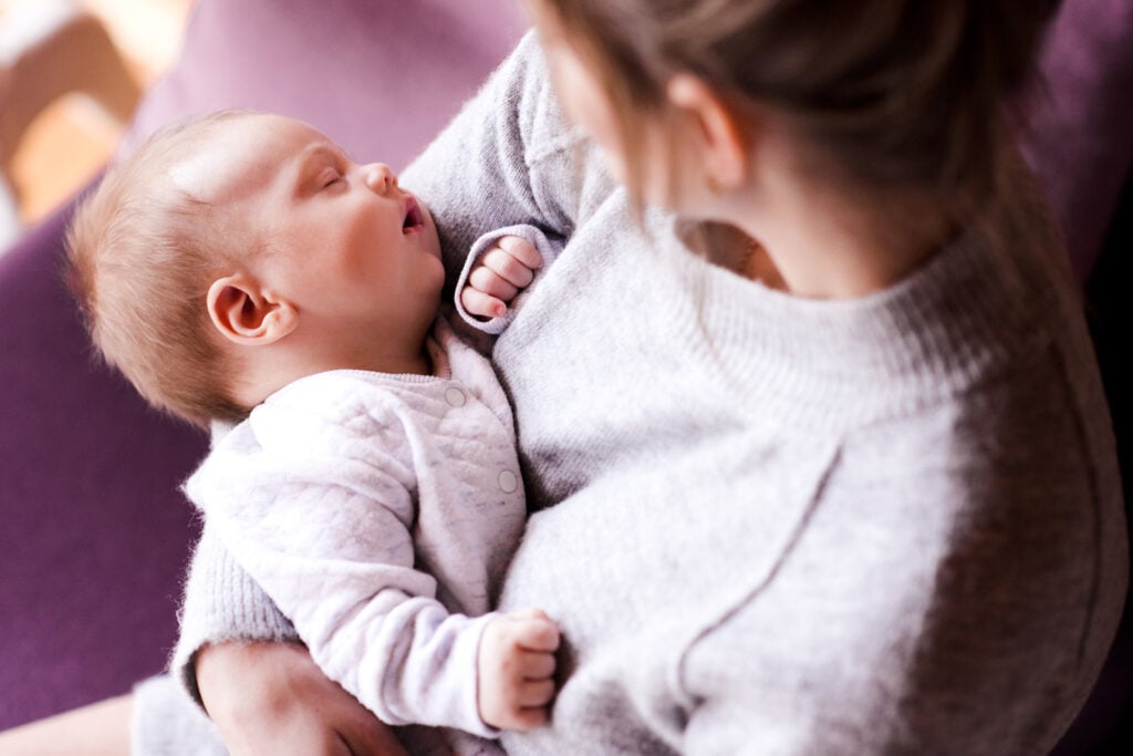 Happy mom holding sleeping baby because she has sleep training help for her newborn from The Peaceful Sleeper. 