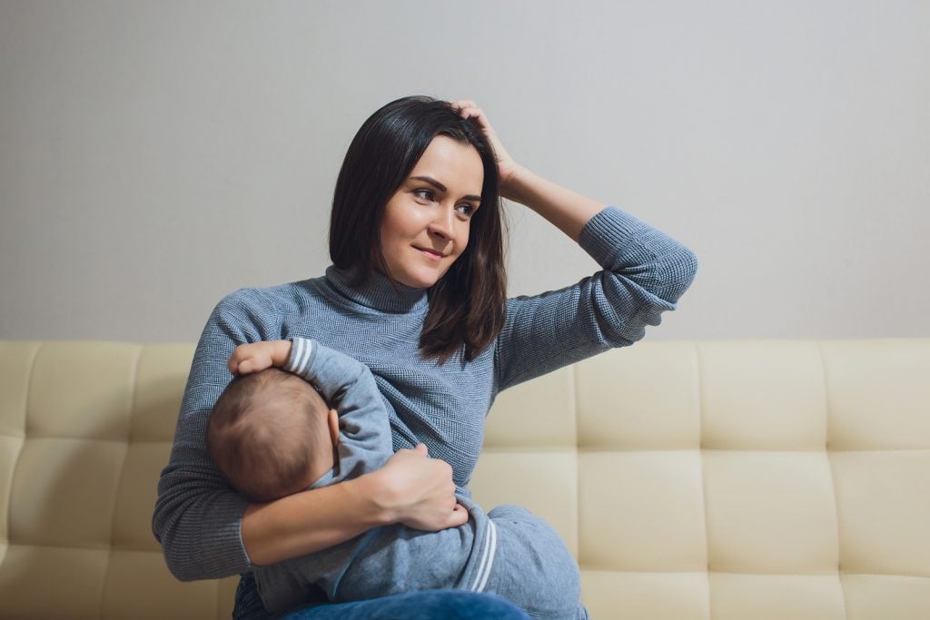 Mother breastfeeding baby, looking confused about so much different advice about crying it out and sleep training. Expert advice from the Peaceful Sleeper.