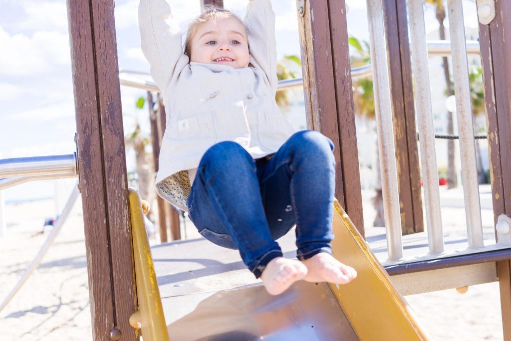 Toddler child wearing jacket playing on slide with confidence and autonomy. The Peaceful Sleeper helps promote calm and confidence when kids can self-soothe and self-regulate appropriately.
