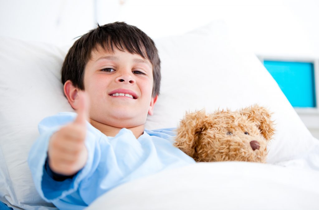 Little boy in hospital bed with teddy bear, giving a thumbs-up to the camera. Professional sleep consultants provide the benefit of a broad lens that can help your family get more sleep. The Peaceful Sleeper Blog explores unexpected benefits of hiring a sleep consultant.