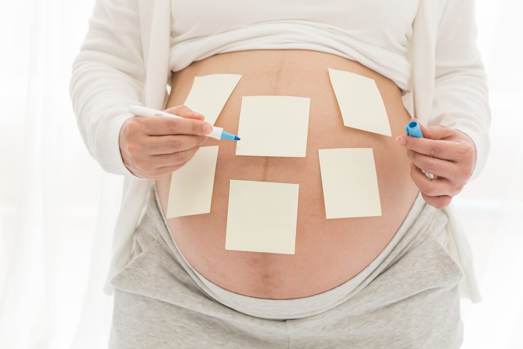 Photo of a pregnant mother's belly with post it notes to represent the different sleep training methods a sleep consultant might suggest for an infant or toddler
