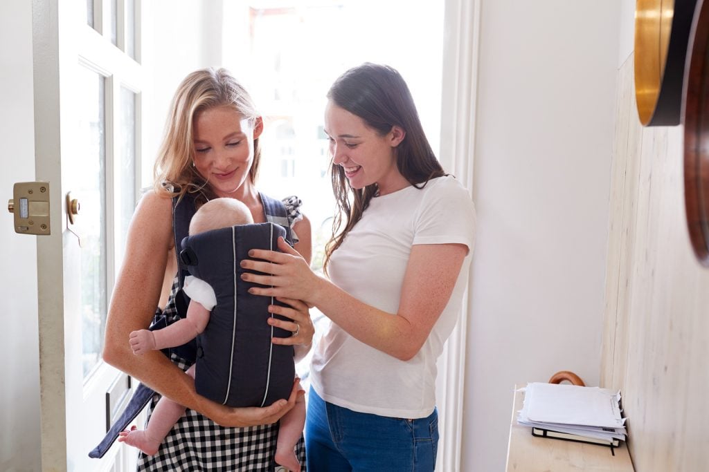 Two women with a baby in a carrier, assisting with professional sleep training for executive mommy | Benefits and traits of hiring expert sleep training help
