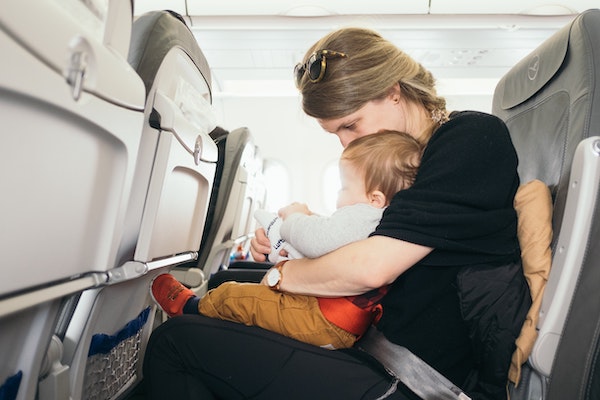 a baby in his mothers arms traveling on an airplane | The Peaceful Sleeper 